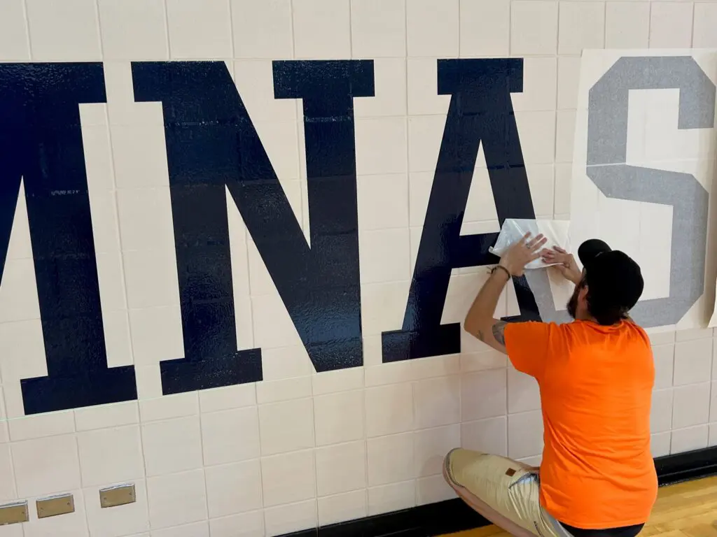 a person in an orange shirt painting a wall with blue letters
