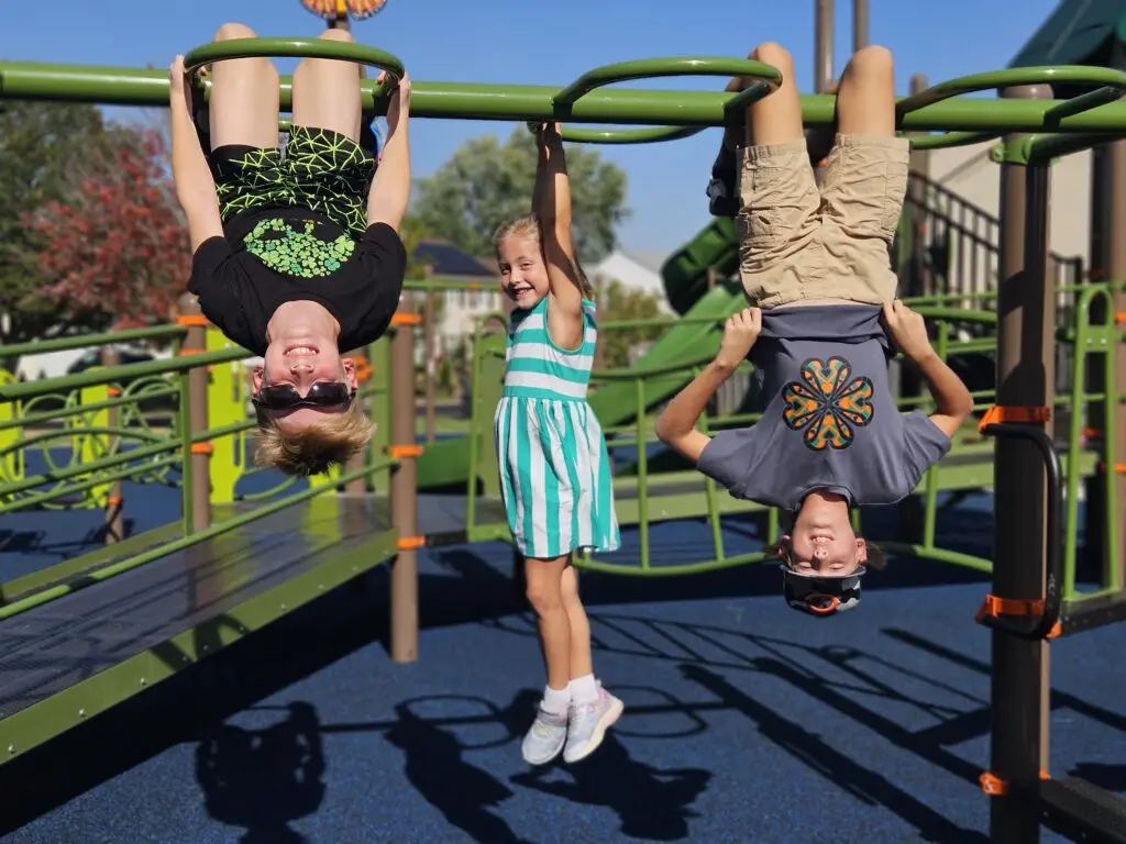 a group of kids from a green metal monkey bars at a playground