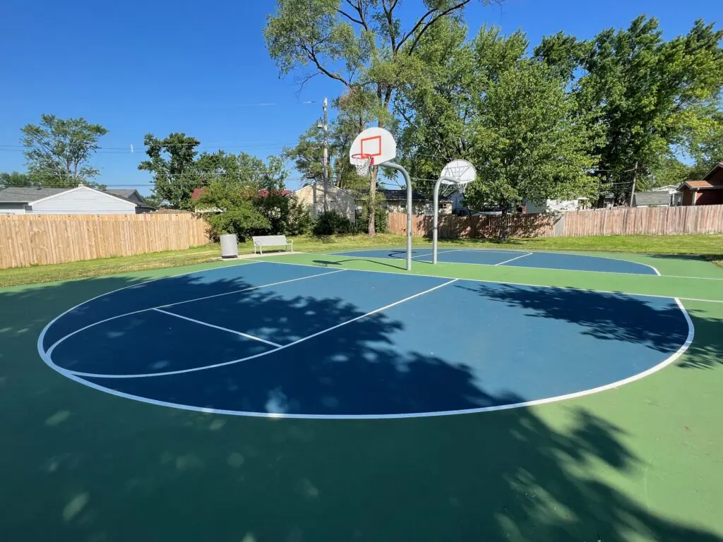 a basketball court with a fence and trees in the background