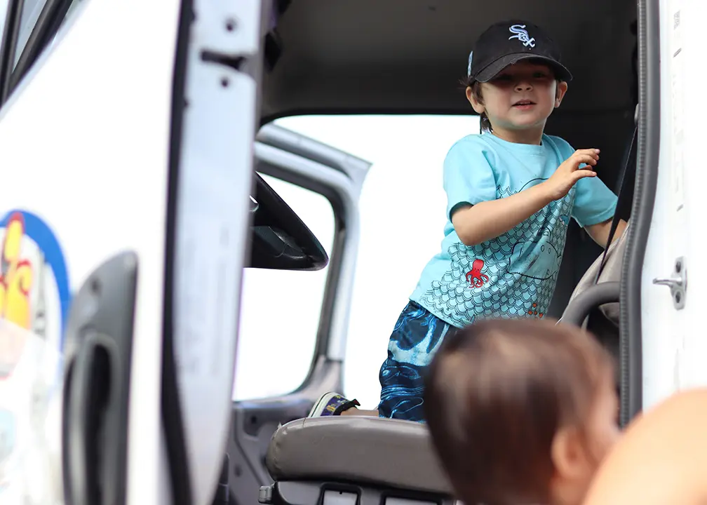 young kid wearing a baseball cap sitting in the cab of a truck