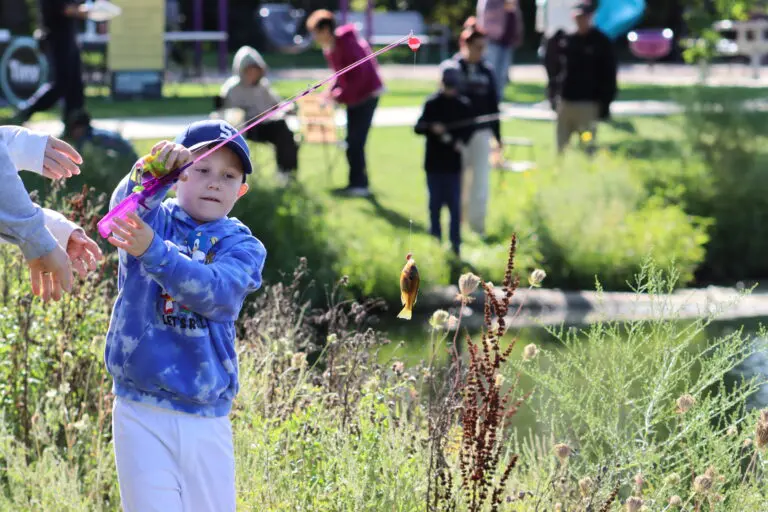 boy in blue sweatshirt and hat holding up a fishing pole with a small fish on the hook
